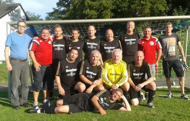Gruppe von Männern posiert fröhlich vor einem Fußballtor für ein Erinnerungsfoto