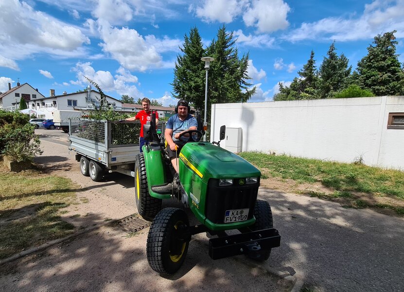 Zwei Menschen sitzen auf einem Traktor und fahren durch einen Hof