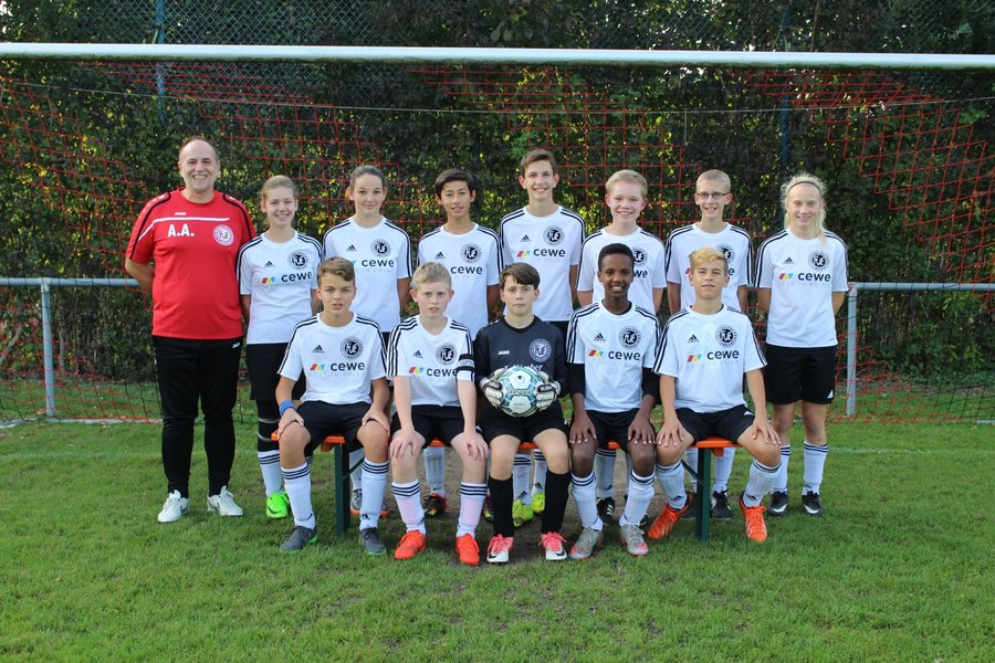 Eine Fußballmannschaft posiert für ein Gruppenfoto, alle Spieler in einheitlichen Trikots und lächelnd in die Kamera.
