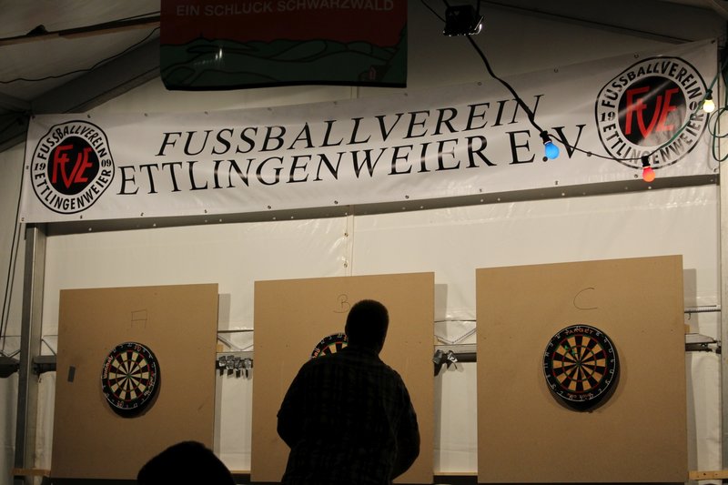 Mann vor einer Dartscheibe, im Hintergrund ein Banner mit der Aufschrift Fussballverein