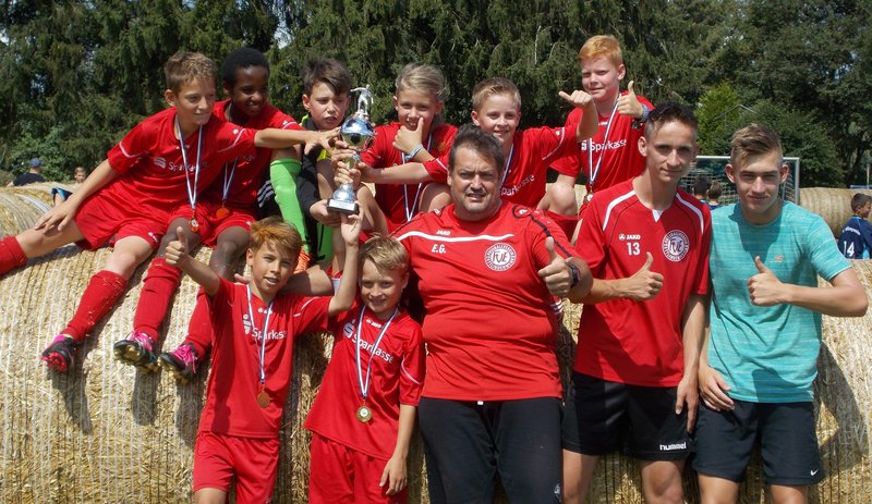 Eine Gruppe von Jungen in roten Fußballtrikots hält stolz ihre Trophäen in die Höhe.