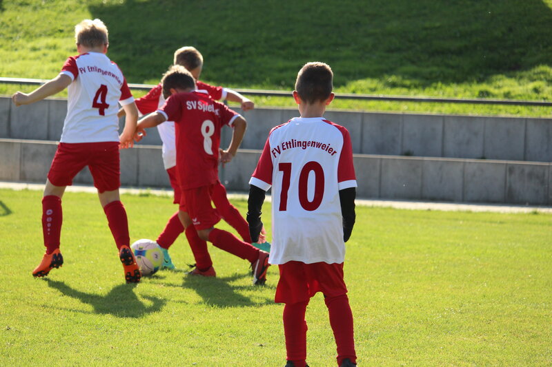 Eine Gruppe junger Fußballspieler in roten und weißen Trikots, die auf einem Rasenplatz trainieren, wobei der Spieler mit der Nummer 10 im Mittelpunkt steht.