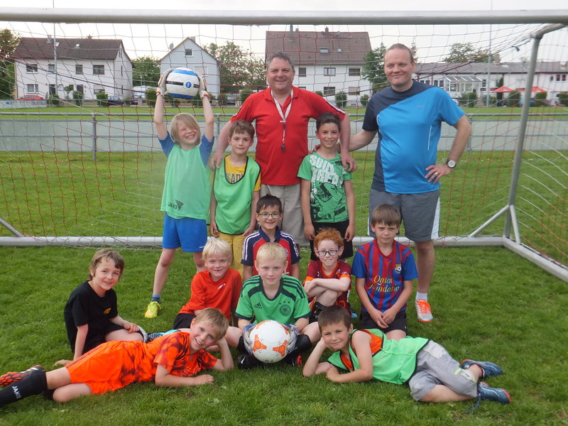 Kinder stehen lächelnd vor einem Fußballtor und posieren für ein Gruppenfoto.