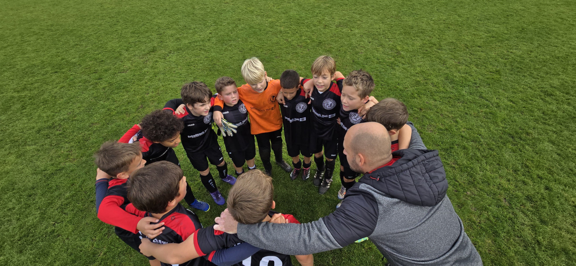 Eine Jugendfußballmannschaft versammelt sich vor ihrem Spiel auf einer Wiese, um Teamgeist und Kameradschaft zu zeigen.