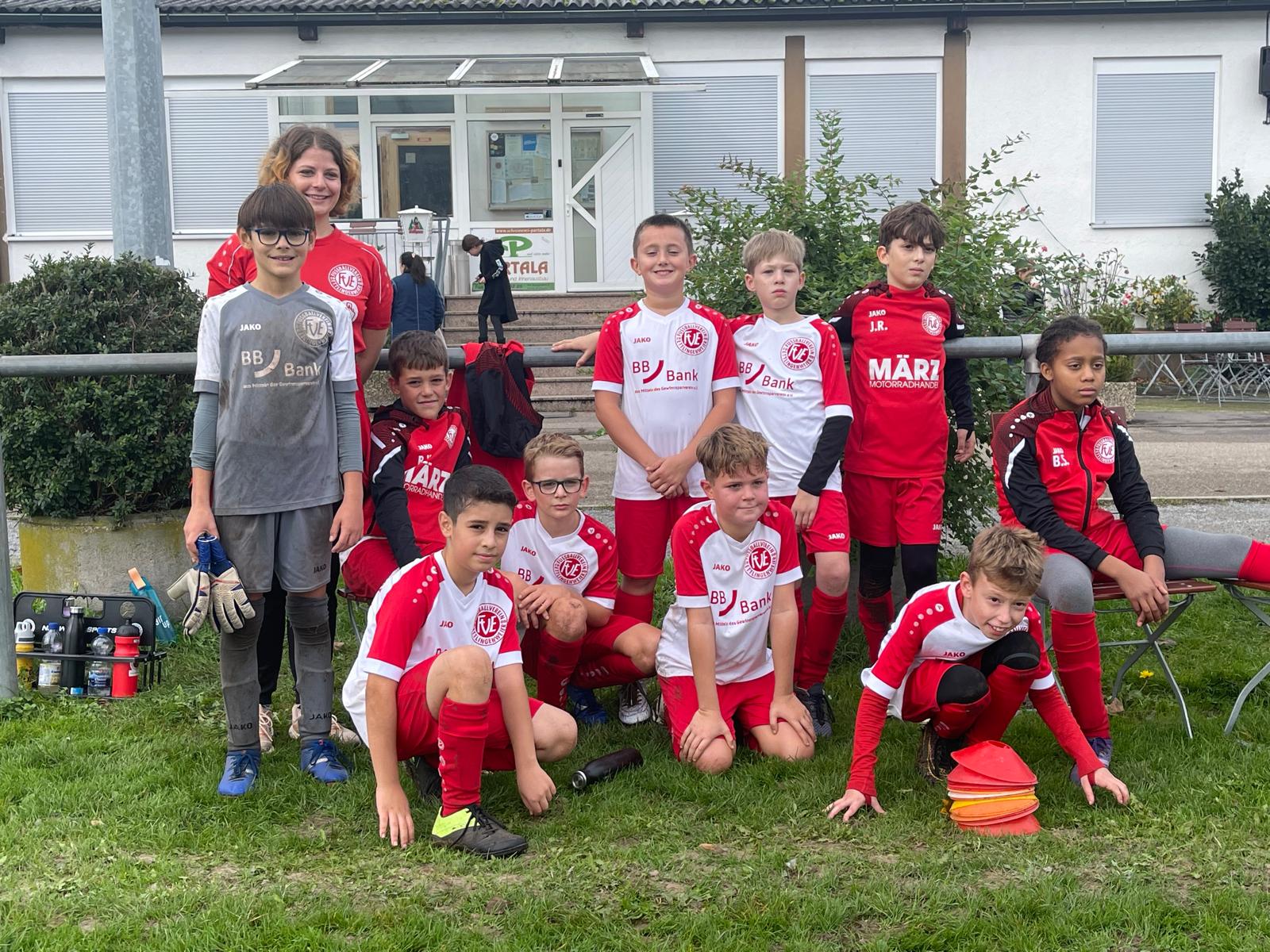 Eine Jugendfußballmannschaft posiert gemeinsam im Freien, in rot-weißen Trikots, mit Torwartausrüstung im Vordergrund.