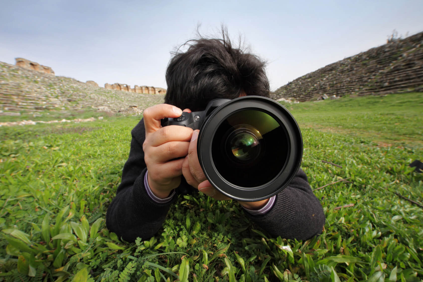 Ein Mann fotografiert mit einer Kamera im Gras, während er die Schönheit der Natur festhält.