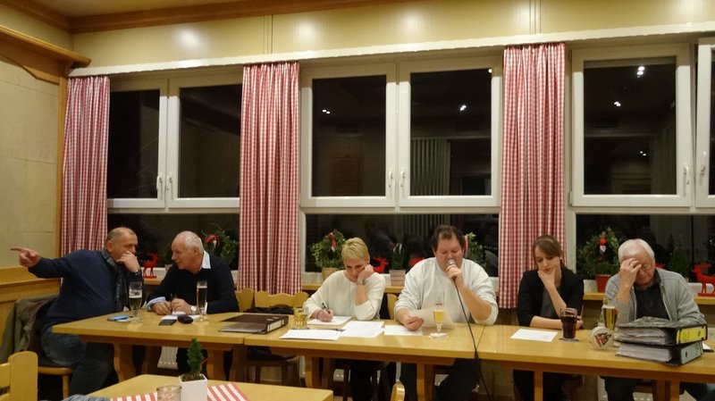Eine Gruppe von Menschen, die an einem langen Tisch mit Notizbüchern und Getränken in einem warm beleuchteten Raum mit karierten Vorhängen sitzen und diskutieren.