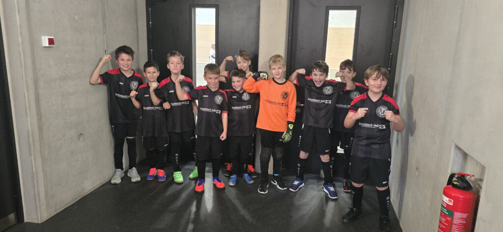 Eine Gruppe junger Fußballspieler in schwarz-roten Trikots posiert selbstbewusst vor einem Tor und demonstriert so ihren Teamgeist.