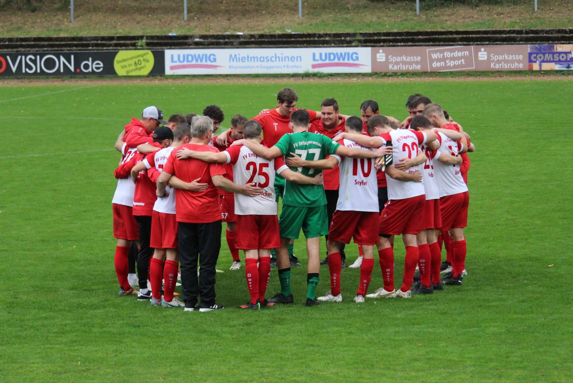 Eine Gruppe von Männern steht im Kreis auf einem Fußballfeld und diskutiert angeregt