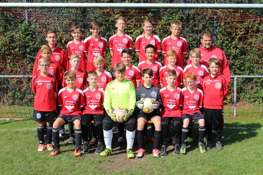 Eine Jugendfußballmannschaft in roten Trikots posiert für ein Gruppenfoto auf einer Wiese mit einem Netztor im Hintergrund.