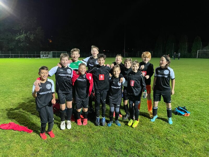 Eine Gruppe junger Fußballspieler in schwarz-roten Trikots posiert nachts auf einer Wiese, um ihre Teamarbeit zu feiern.