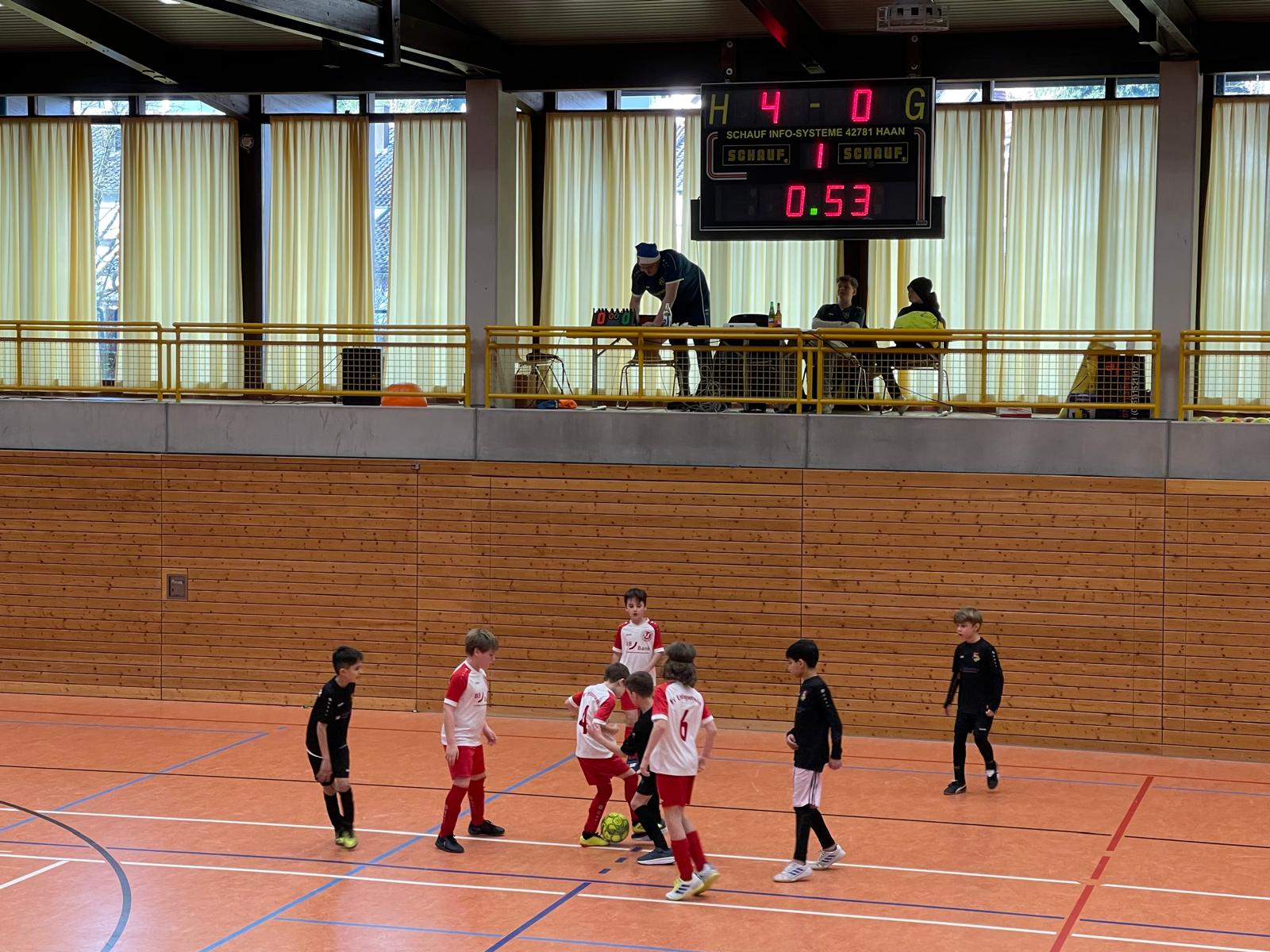 Ein Jugend-Futsal-Spiel mit Spielern in roten und schwarzen Trikots und einem Spielstand von 4:0 auf der Anzeigetafel.