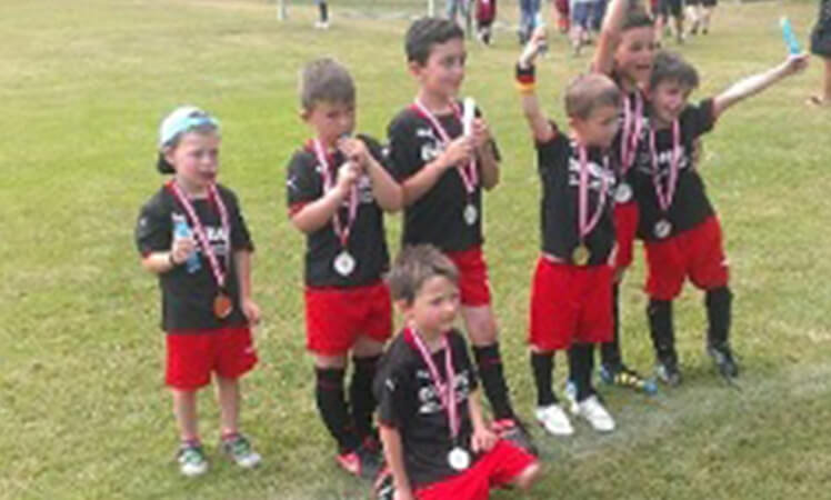 Kinder in Fußballtrikots halten freudig ihre Medaillen in der Hand und feiern gemeinsam ihre Leistung.
