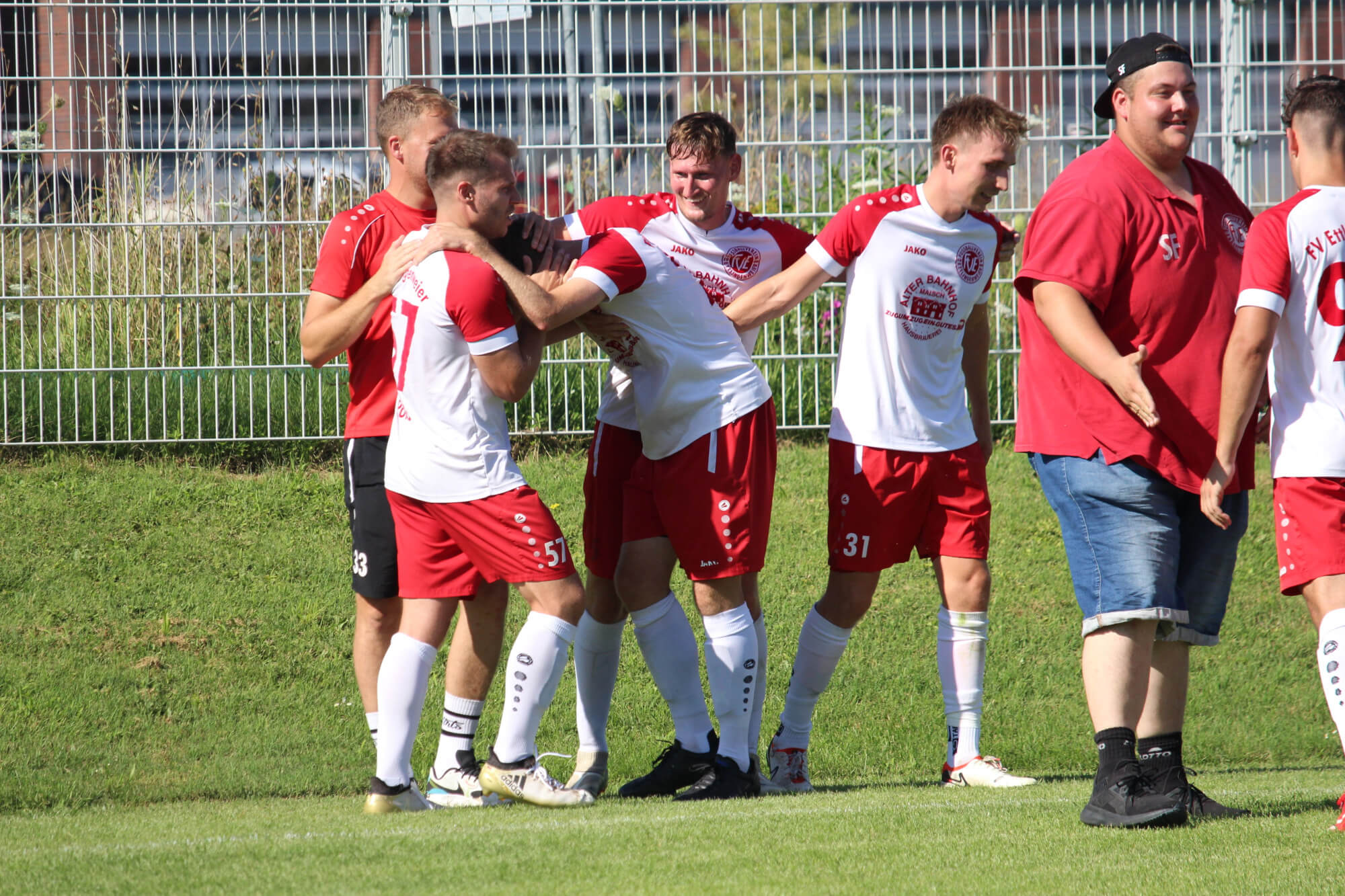 Eine Gruppe von Fußballspielern in rot-weißen Trikots feiert gemeinsam auf einer Wiese und demonstriert Teamwork und Kameradschaft.