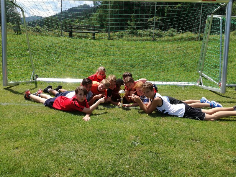 Eine Gruppe von Kindern liegt auf dem Gras neben einem Fußballtor und genießt die Zeit im Freien.