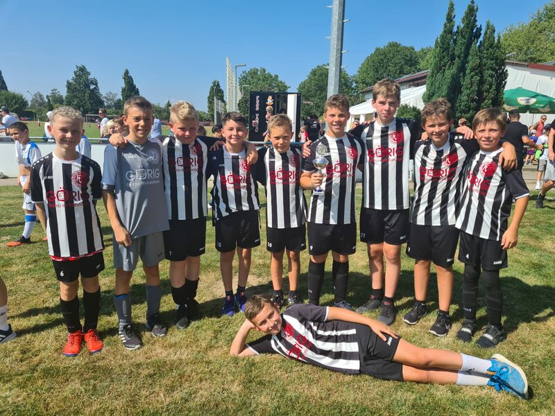 Eine fröhliche Gruppe junger Fußballspieler in schwarz-weiß gestreiften Trikots posiert an einem sonnigen Tag zusammen und feiert ihren Erfolg.