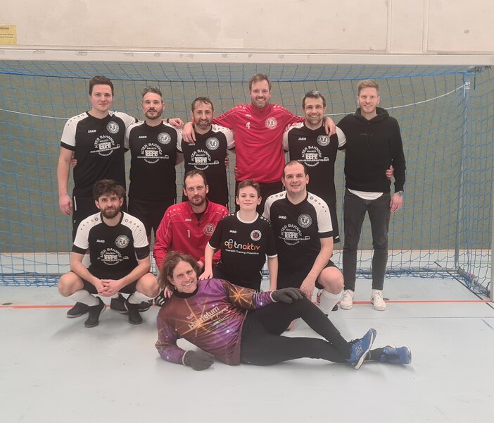 Männer und Frauen stehen gemeinsam auf einem Fußballfeld und lächeln für ein Gruppenfoto.