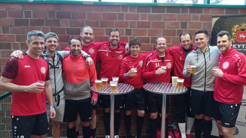 Eine Gruppe von Männern in roten Hemden, die Bier halten und gemeinsam eine fröhliche Zeit verbringen.