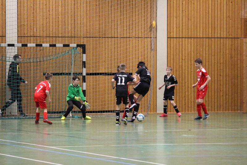 Ein Jugend-Futsal-Spiel in Aktion: Spieler in schwarzen und roten Trikots kämpfen in der Nähe des Tores um den Ball.